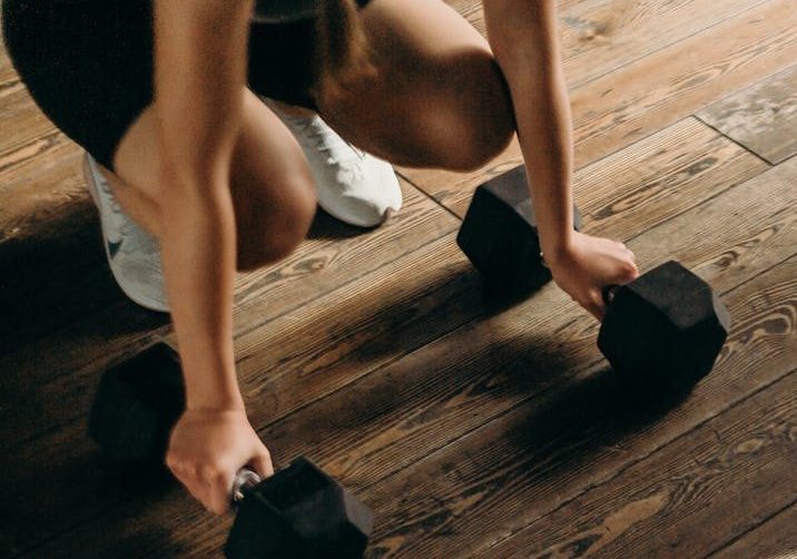 Female gym-goer in action with dumbbells on wooden floor, ready to lift.